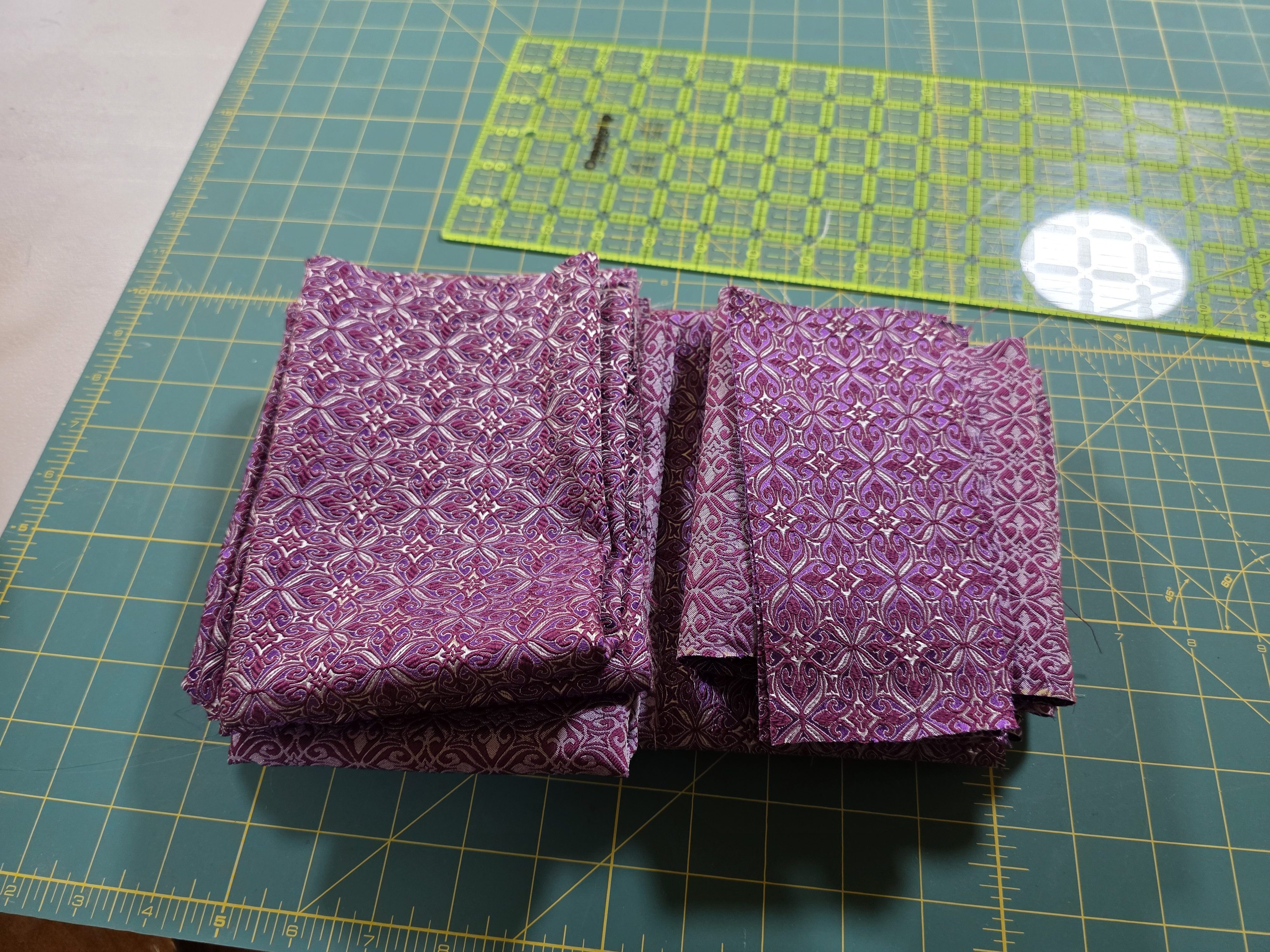 Noble brocade, burgundy-silver-violet from Sartor folded on a green olfa cutter mat with a clear quilting ruler beside it
