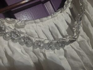 Close of body linen neckline with metallic silver and faux pearl tirm with a silver cord edging the pleats.  